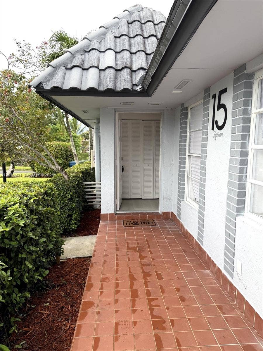 301 Bonaventure Boulevard, #15, Weston, FL 33326 Covered entryway featuring terra cotta tile flooring, a hipped roofline with concrete tiles, white louvered entry doors, and contrasting painted brick accents