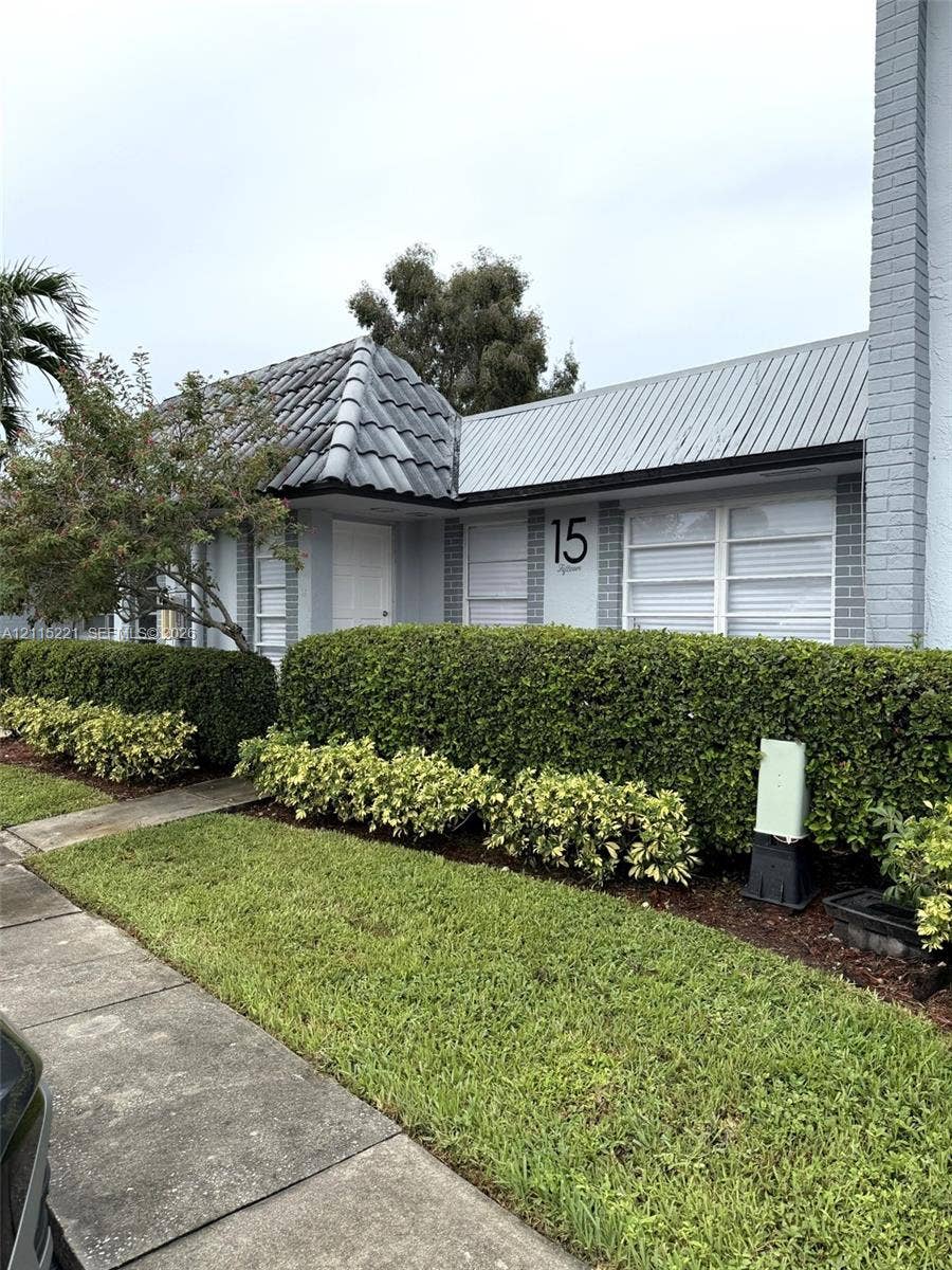 301 Bonaventure Boulevard, #15, Weston, FL 33326 Exterior featuring gray brick facade, dark tile roofing, metal shed-style roofing accents, and manicured landscaping