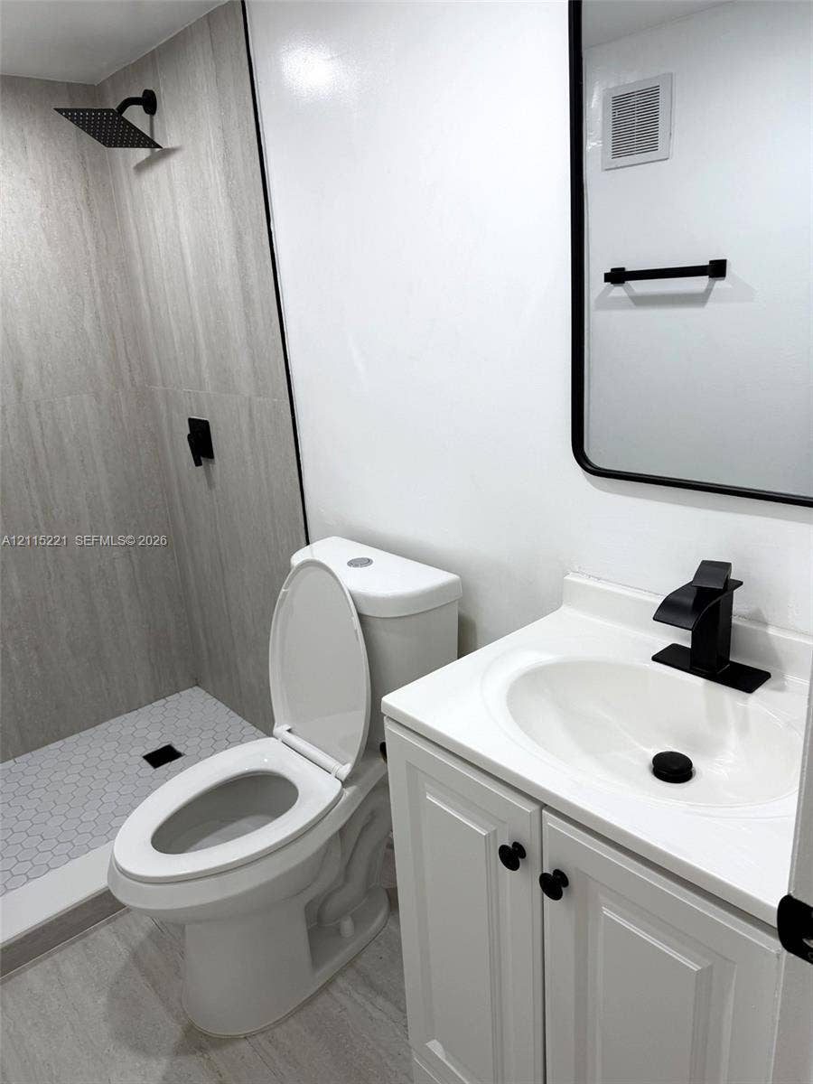 301 Bonaventure Boulevard, #15, Weston, FL 33326 Bathroom featuring a walk-in shower with large-format wall tile and hexagonal floor tile, a white vanity cabinet, a rectangular mirror with a black frame, and matte black plumbing fixtures