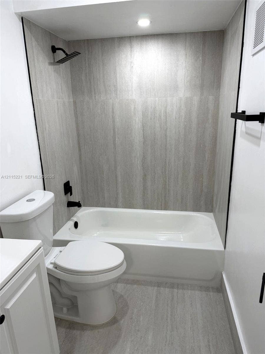 301 Bonaventure Boulevard, #15, Weston, FL 33326 Bathroom featuring a white soaking tub with floor-to-ceiling neutral stone-finish tile surround, a matte black rainfall showerhead, matte black faucet fixtures, and matching matte black towel hardware