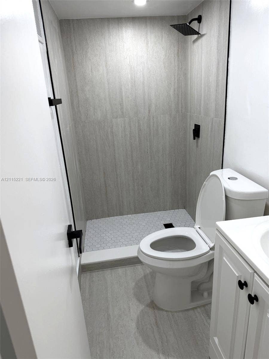 301 Bonaventure Boulevard, #15, Weston, FL 33326 Bathroom featuring a walk-in shower with large-format wall tile and hexagonal floor tile, matte black rainfall shower head, white vanity cabinet, and matte black hardware