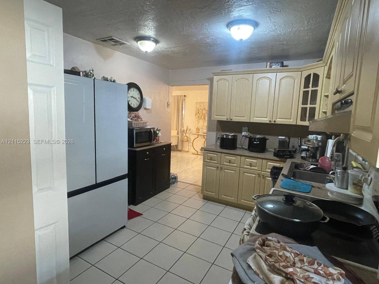 737 SE 8th Place, Hialeah, FL 33010 Kitchen featuring cream-toned cabinetry with glass-panel accents, solid surface countertops, a stainless steel multi-door refrigerator, tile flooring, and dual flush-mount ceiling light fixtures