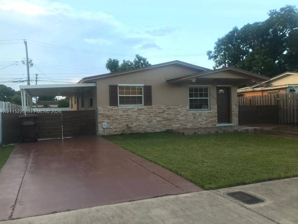 737 SE 8th Place, Hialeah, FL 33010 Single-story exterior featuring a stone veneer facade, covered carport, front lawn, and wooden privacy fencing