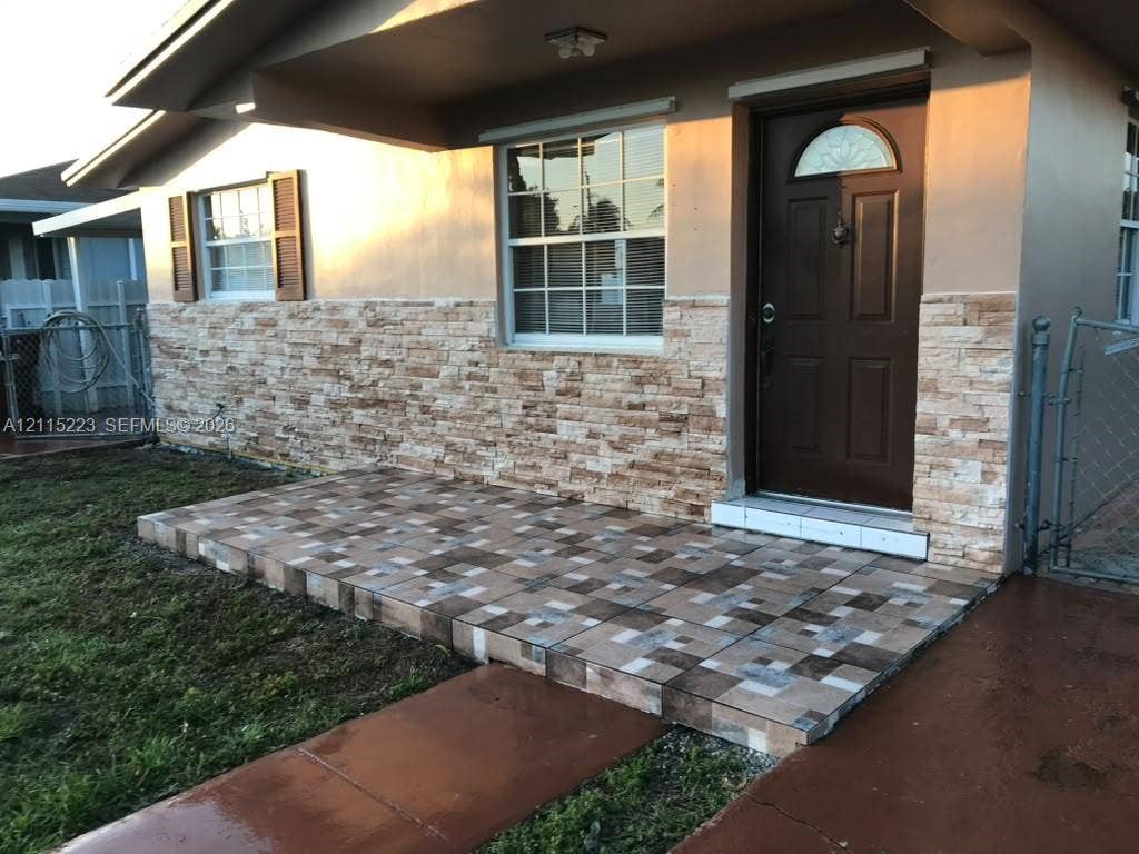 737 SE 8th Place, Hialeah, FL 33010 Exterior entry featuring a textured stone veneer facade, a tiled porch, and an arched-glass entry door with a brass-finish door knocker