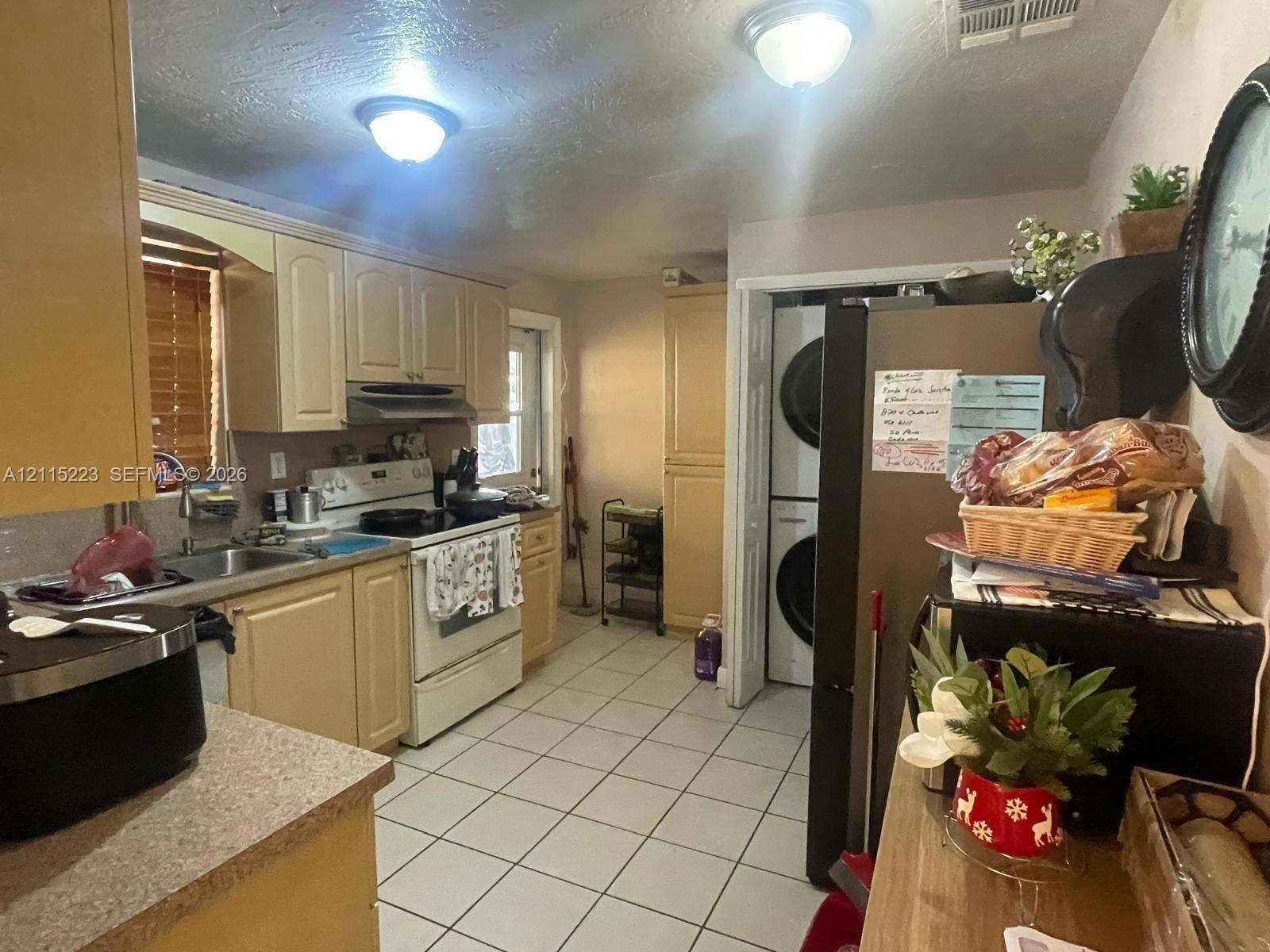 737 SE 8th Place, Hialeah, FL 33010 Kitchen featuring light-toned cabinetry, solid-surface countertops, tile flooring, and a dedicated laundry area with stacked washer and dryer