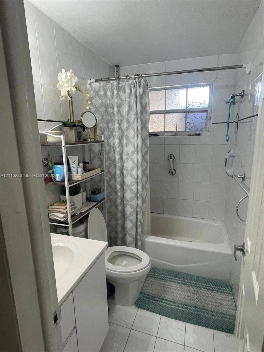 737 SE 8th Place, Hialeah, FL 33010 Bathroom featuring white tile wall cladding with decorative black inlay, a white vanity with an integrated basin, a standard soaking tub, and a window with textured privacy glass