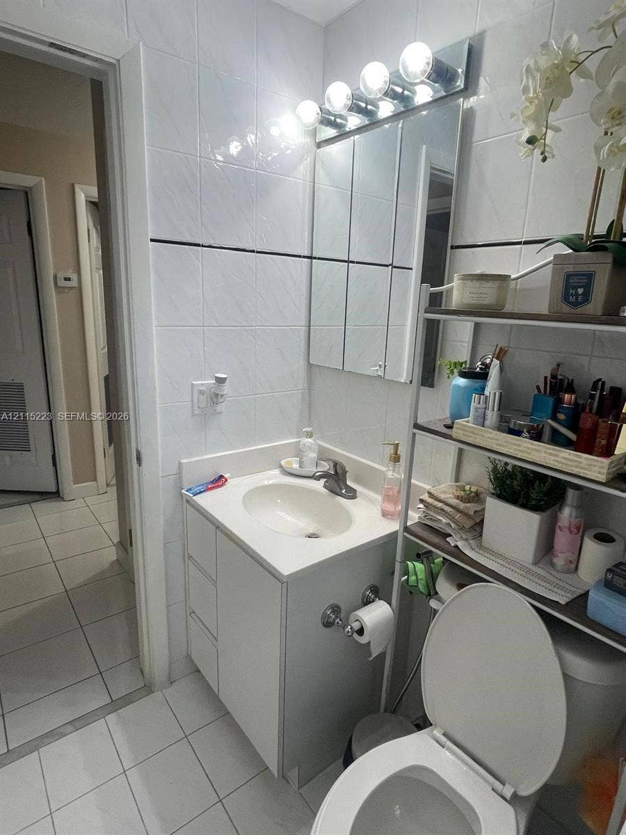 737 SE 8th Place, Hialeah, FL 33010 Bathroom featuring white tiled walls with a horizontal decorative accent, a vanity with a white countertop and integrated sink, a multi-bulb vanity light fixture, and floor tiles