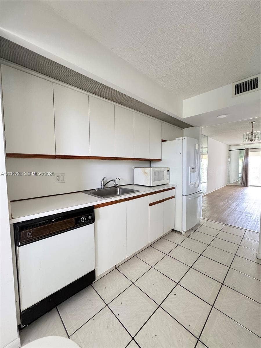 12950 SW 7th Court, #404A, Pembroke Pines, Pembroke Pines, FL 33027 Kitchen featuring white cabinetry, flat-surface countertops, stainless steel sink, tiled flooring, and white kitchen appliances
