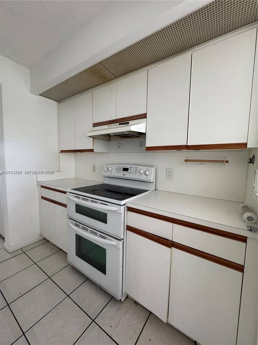 12950 SW 7th Court, #404A, Pembroke Pines, Pembroke Pines, FL 33027 Kitchen featuring white cabinetry with wood trim, solid-surface countertops, a double-oven range with a glass cooktop, an integrated range hood, and tile flooring