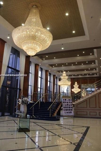 12950 SW 7th Court, #404A, Pembroke Pines, Pembroke Pines, FL 33027 Grand lobby featuring multi-tiered crystal chandeliers, coffered ceilings with recessed lighting, floor-to-ceiling windows, polished stone flooring with decorative inlay, and an open staircase with metal railing