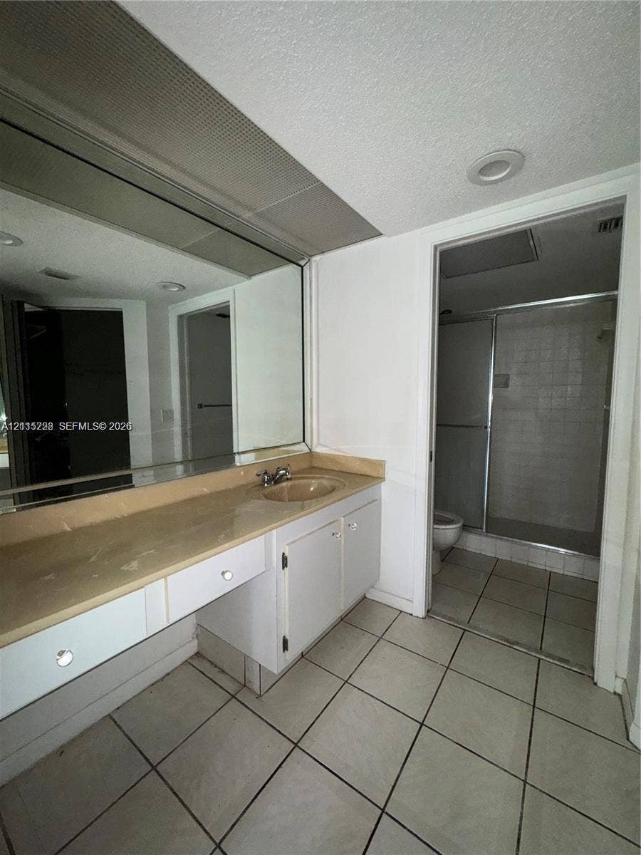 12950 SW 7th Court, #404A, Pembroke Pines, Pembroke Pines, FL 33027 Bathroom featuring a vanity with an integrated sink, expansive wall-mounted mirror, ceramic tile flooring, and a walk-in shower enclosure