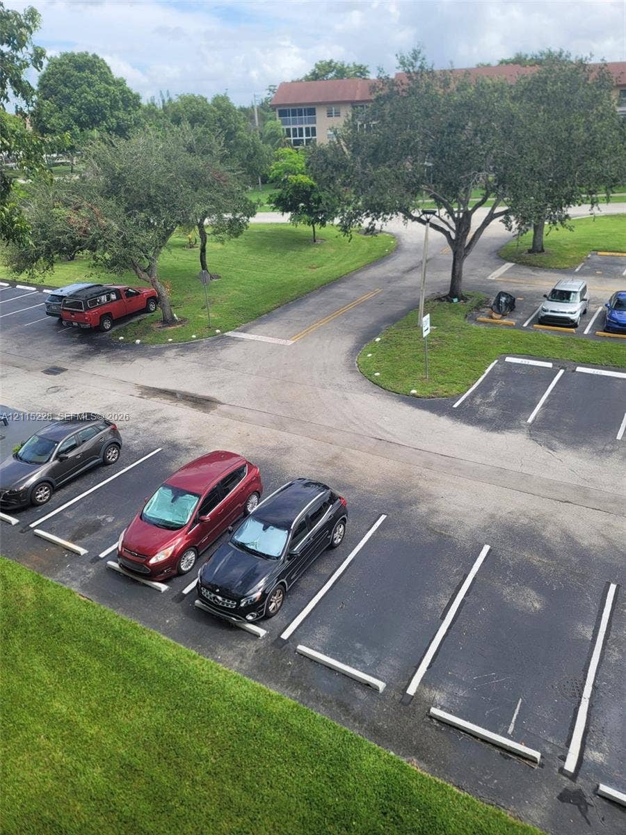 12950 SW 7th Court, #404A, Pembroke Pines, Pembroke Pines, FL 33027 Asphalt parking area with designated stalls, mature trees, and landscaped green space