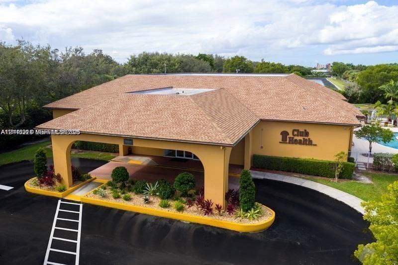 12950 SW 7th Court, #404A, Pembroke Pines, Pembroke Pines, FL 33027 Exterior perspective of the facility featuring a covered porte-cochre, a shingled hipped roof, paved circular driveway, and curated perimeter landscaping