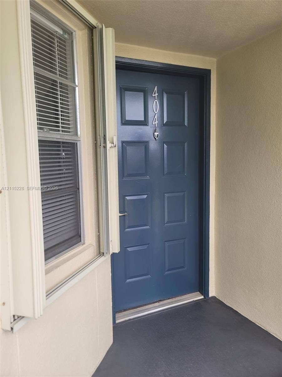 12950 SW 7th Court, #404A, Pembroke Pines, Pembroke Pines, FL 33027 Blue paneled door featuring metallic house numbers and a silver-finish handle set, paired with a vertical-slider window with integrated mini-blinds