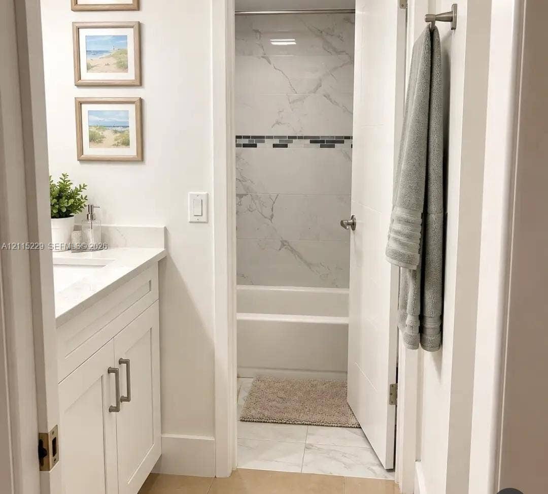 2020 NE 135th Street, #211, North Miami, FL 33181 White shaker-style vanity with a light-toned solid surface countertop and undermount sink, complemented by large-format light-toned tile flooring and a tub-shower enclosure featuring decorative mosaic tile accents