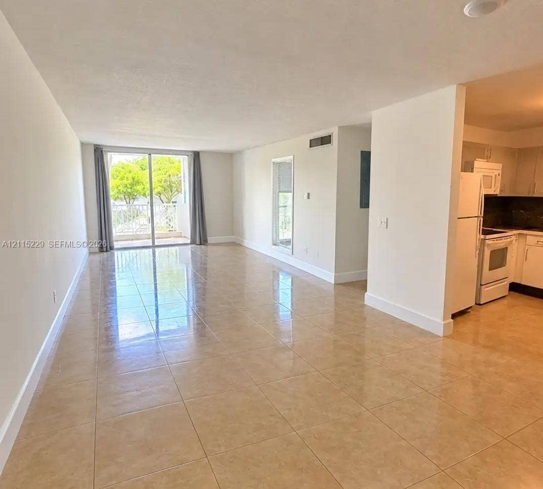 2020 NE 135th Street, #211, North Miami, FL 33181 Open-concept area featuring oversized ceramic tile flooring, sliding glass door access to a balcony, and white cabinetry with built-in appliances