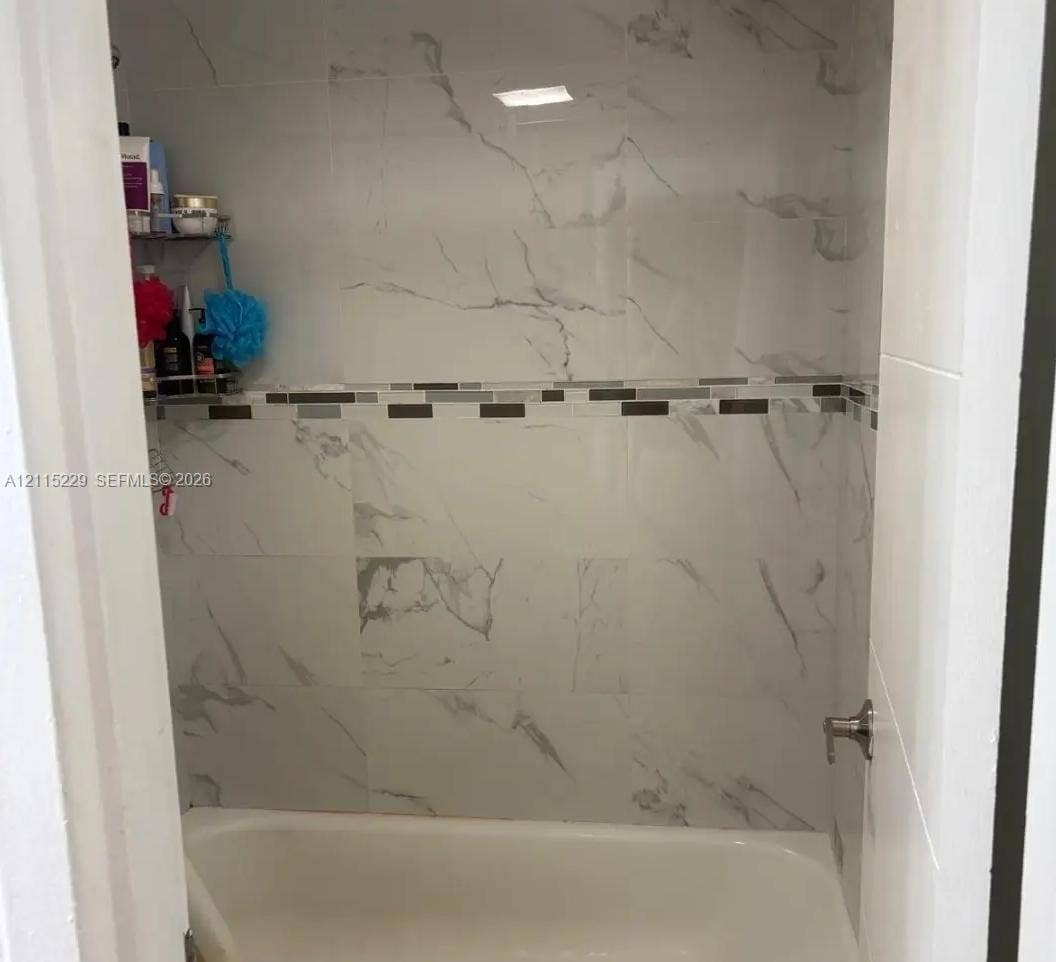 2020 NE 135th Street, #211, North Miami, FL 33181 Full-height wall tiling with a vein-patterned finish, complemented by a horizontal decorative mosaic tile border and a standard bathtub fixture