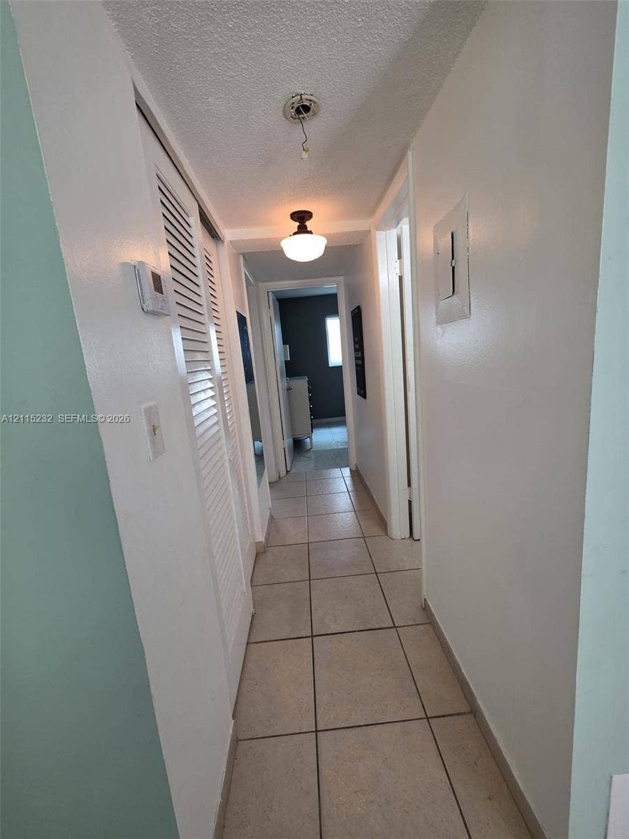 Hallway featuring ceramic tile flooring, built-in louvered-door closet, and semi-flush mount ceiling lighting