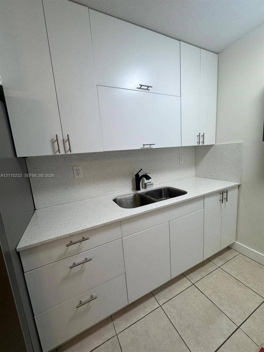 Flat-panel white cabinetry featuring stainless steel bar pulls, stone-composite countertop, matching full-height backsplash, undermount double-basin stainless steel sink, and matte black high-arc faucet
