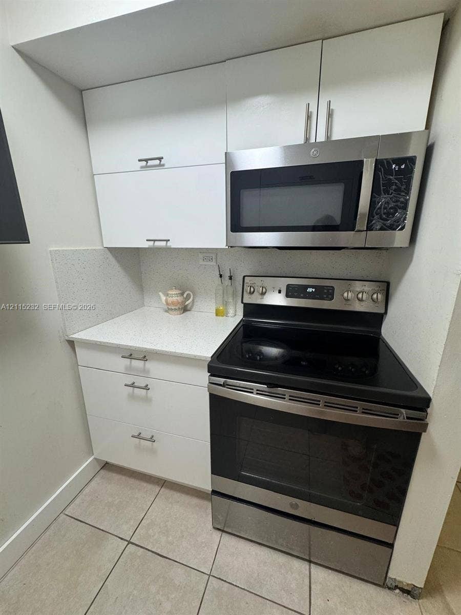 White flat-panel cabinetry featuring brushed nickel pulls, stone-composite countertops, and a built-in stainless steel microwave and range