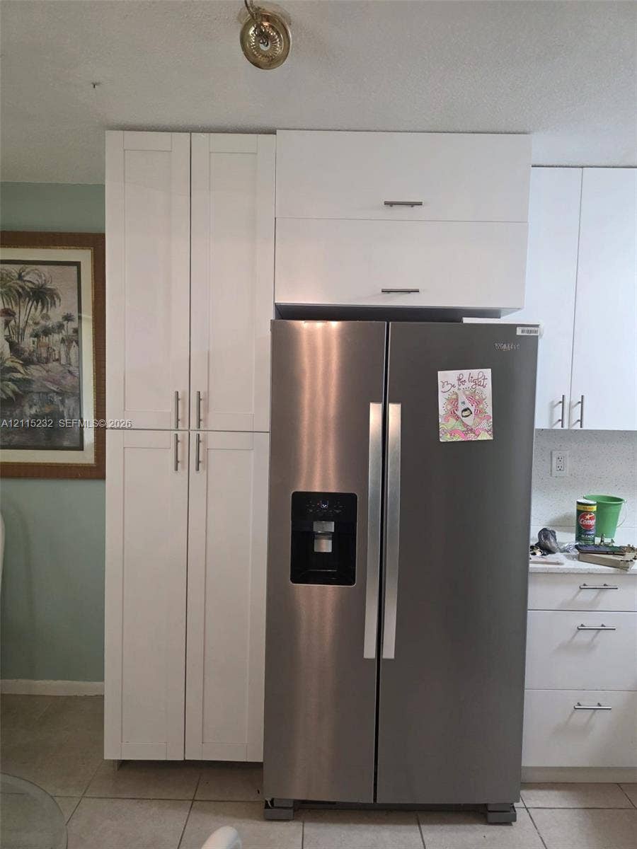 White shaker-style cabinetry with matte silver hardware, floor-to-ceiling pantry storage, and stainless steel side-by-side refrigerator