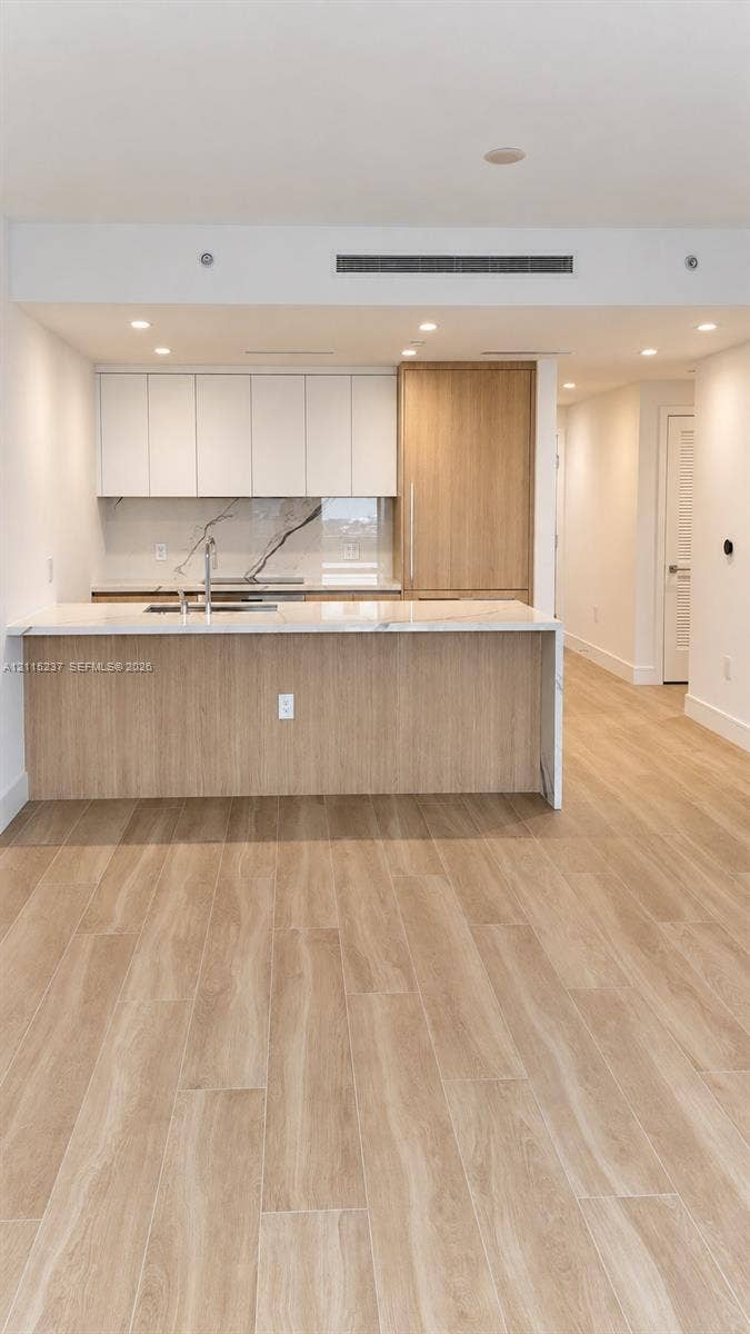 2411 Laguna Circle, #802, North Miami, North Miami, FL 33181 Kitchen featuring flat-panel cabinetry, light-tone wood-finish island, stone-surface countertops, stone-patterned backsplash, and wood-finish flooring