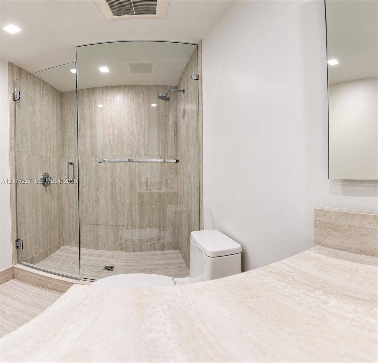 2411 Laguna Circle, #802, North Miami, North Miami, FL 33181 Walk-in shower with a curved glass enclosure and stone-finish wall tile, complemented by a stone-finish vanity countertop and a wall-mounted mirror