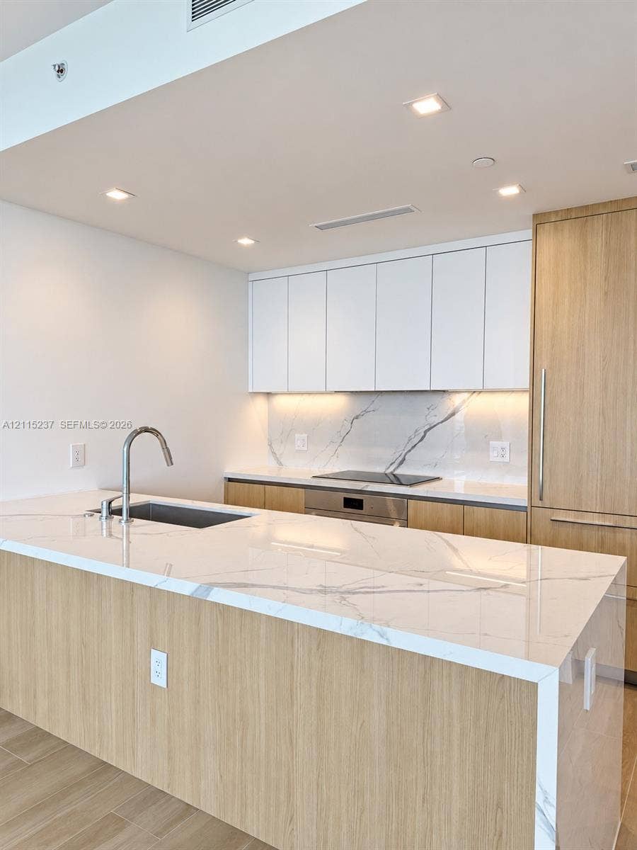 2411 Laguna Circle, #802, North Miami, North Miami, FL 33181 Kitchen featuring a waterfall-edge stone countertop, wood-finish cabinetry, integrated appliances, under-cabinet lighting, and a stone slab backsplash