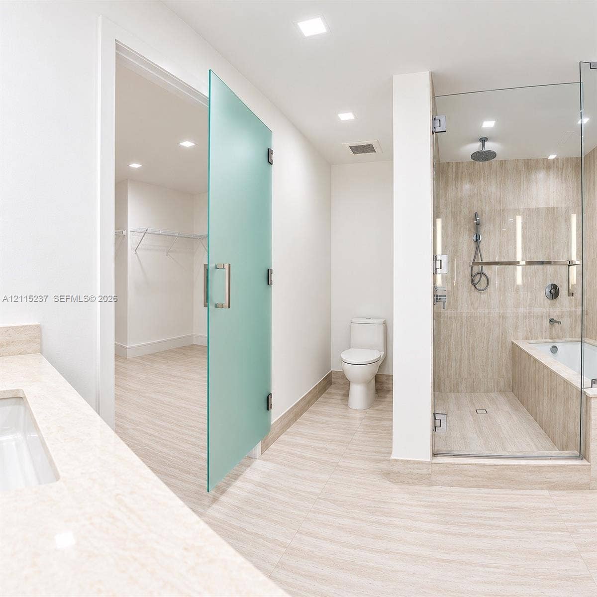 2411 Laguna Circle, #802, North Miami, North Miami, FL 33181 Bathroom featuring stone-finish floor and wall tiles, glass-enclosed shower with integrated tub, frosted glass door, and neutral-toned countertop with an undermount sink