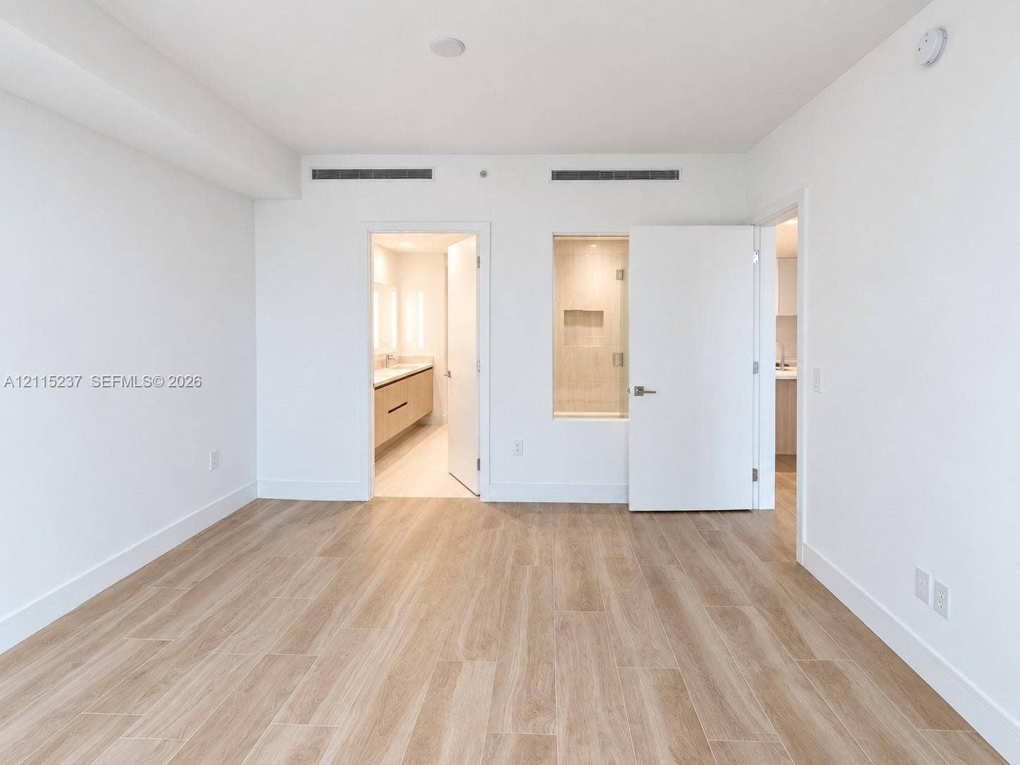 2411 Laguna Circle, #802, North Miami, North Miami, FL 33181 Interior space featuring light-toned wood-finish flooring, white walls, minimalist door hardware, and a fixed glass window panel