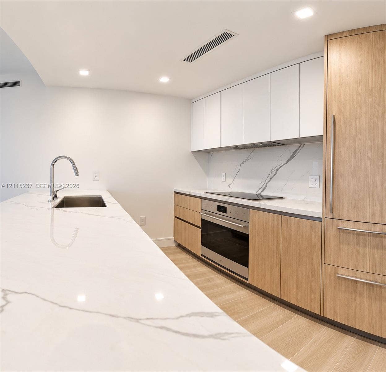 2411 Laguna Circle, #802, North Miami, North Miami, FL 33181 Kitchen featuring an expansive stone countertop with integrated sink, wood-finish cabinetry, white matte upper cabinets, stone backsplash with veining, and stainless steel built-in appliances