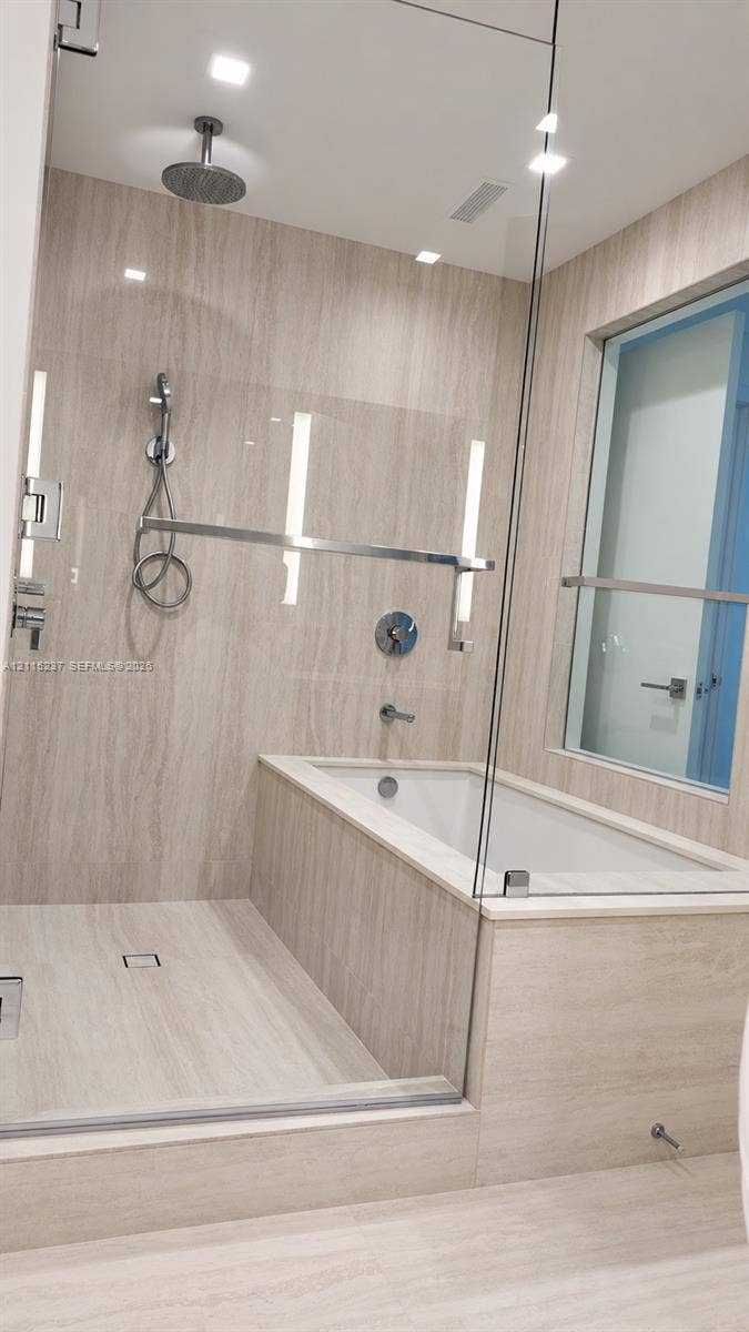 2411 Laguna Circle, #802, North Miami, North Miami, FL 33181 Glass-enclosed wet room featuring a built-in soaking tub, ceiling-mounted rainfall showerhead, handheld shower fixture, and floor-to-ceiling stone-finish tile surround