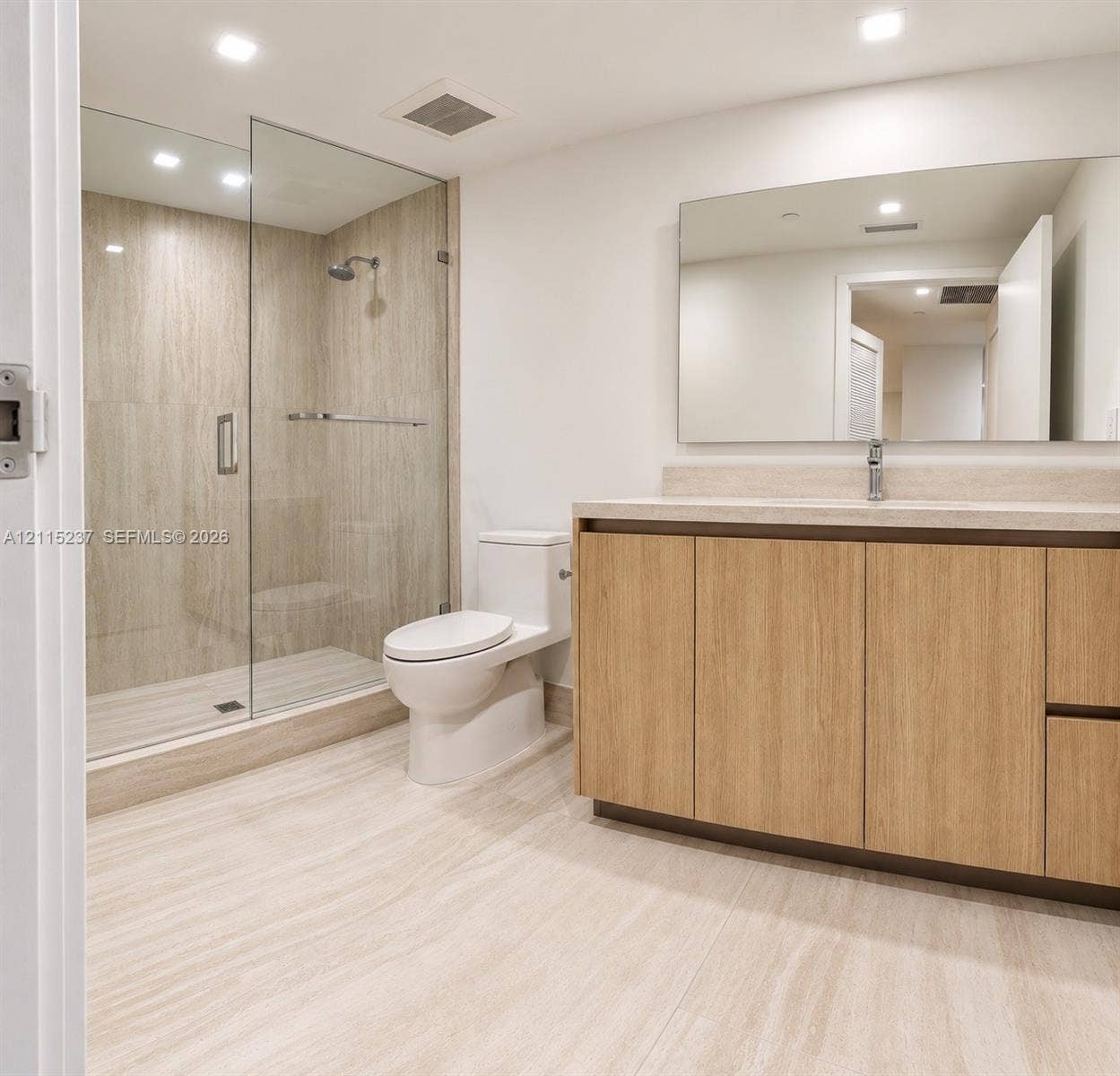 2411 Laguna Circle, #802, North Miami, North Miami, FL 33181 Bathroom featuring a glass-enclosed walk-in shower with tile surround, wood-finish cabinetry, stone-surface countertop, and a wide-format wall mirror
