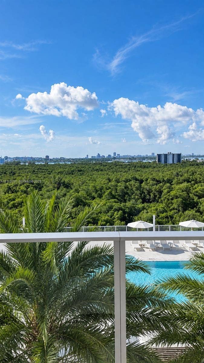 2411 Laguna Circle, #802, North Miami, North Miami, FL 33181 Private balcony with a metal and glass railing, featuring an elevated outlook of a swimming pool, palm trees, and dense forest canopy