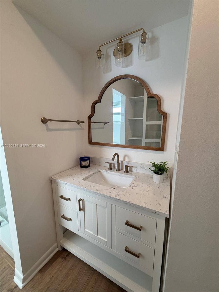 9015 SW 138th Street, #16-2, Miami, Miami, FL 33176 White vanity with stone-look countertop, undermount sink, brass-finish hardware, three-light wall-mounted fixture, and arched decorative mirror
