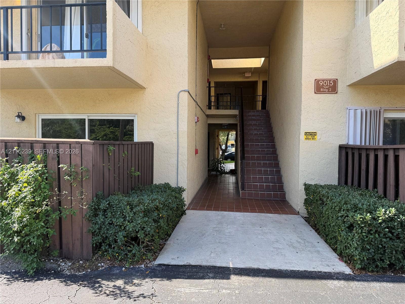 9015 SW 138th Street, #16-2, Miami, Miami, FL 33176 Stucco exterior featuring private balconies with metal railings, dark wood privacy fencing, a tile-paved staircase, and concrete ground-level entryway