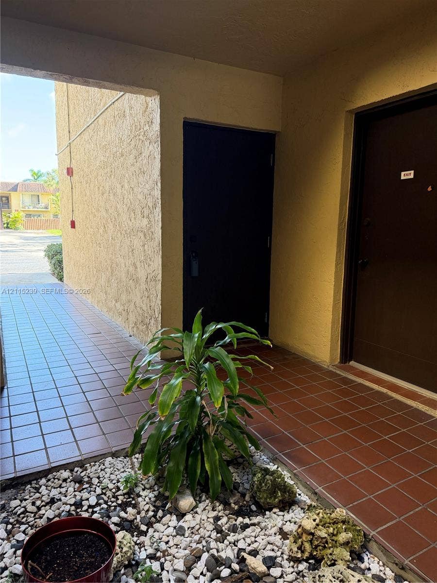 9015 SW 138th Street, #16-2, Miami, Miami, FL 33176 Covered exterior entryway featuring square ceramic floor tiling, stucco wall finishes, and a decorative rock landscape border
