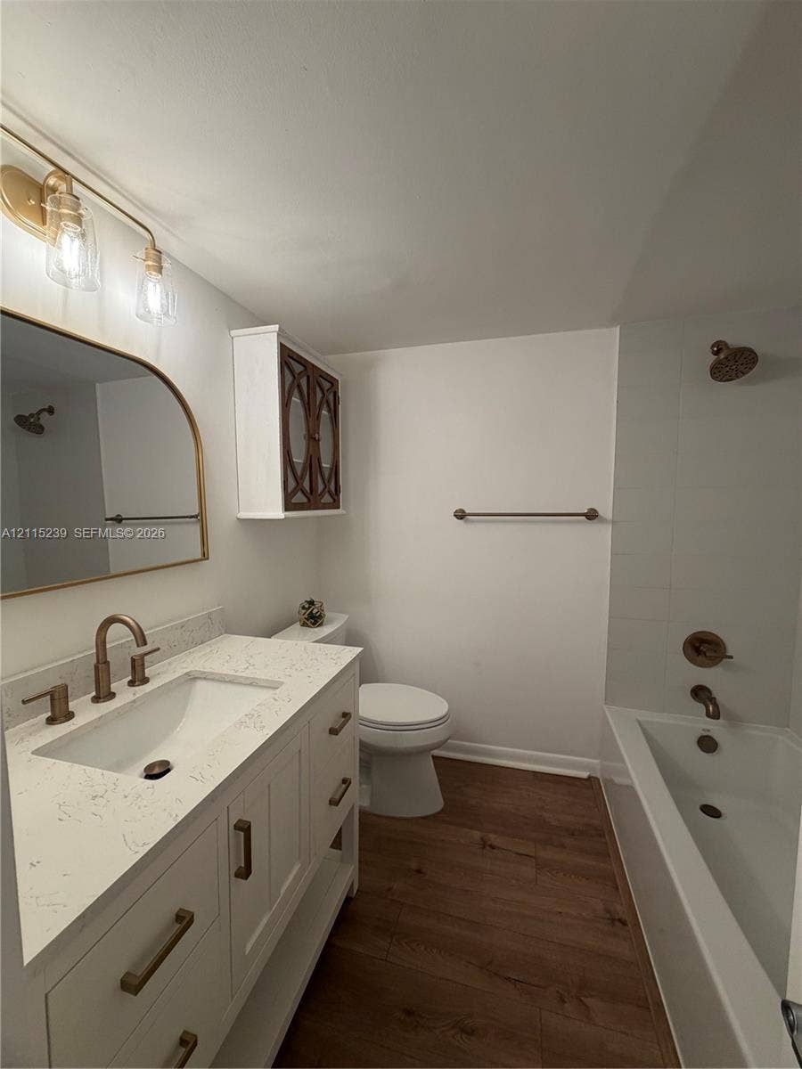 9015 SW 138th Street, #16-2, Miami, Miami, FL 33176 Bathroom featuring a white vanity with a stone countertop, an arched mirror, metallic fixtures, wood-finish flooring, and a shower-tub combination with tile surround