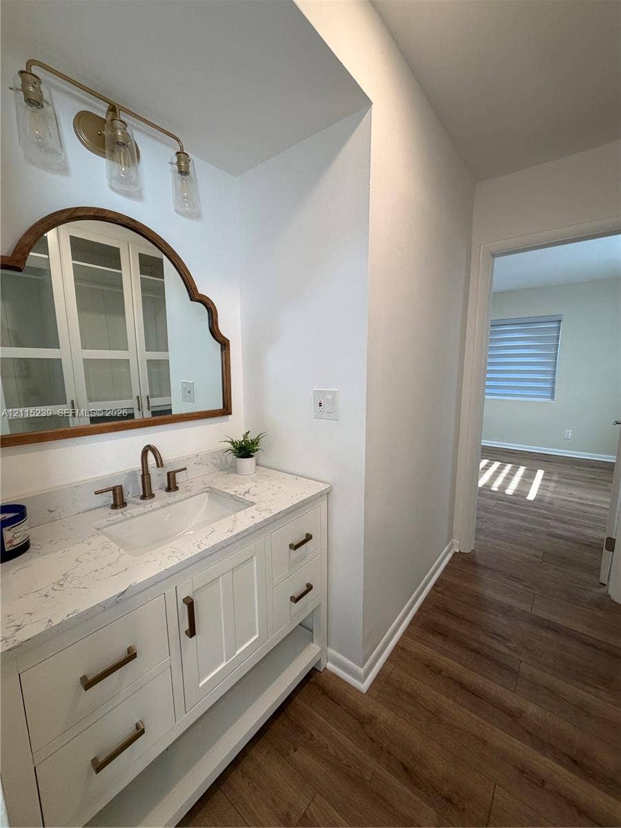 9015 SW 138th Street, #16-2, Miami, Miami, FL 33176 White vanity cabinet with stone countertop and integrated sink, arch-top mirror with wood frame, metallic fixtures, and overhead three-bulb vanity light