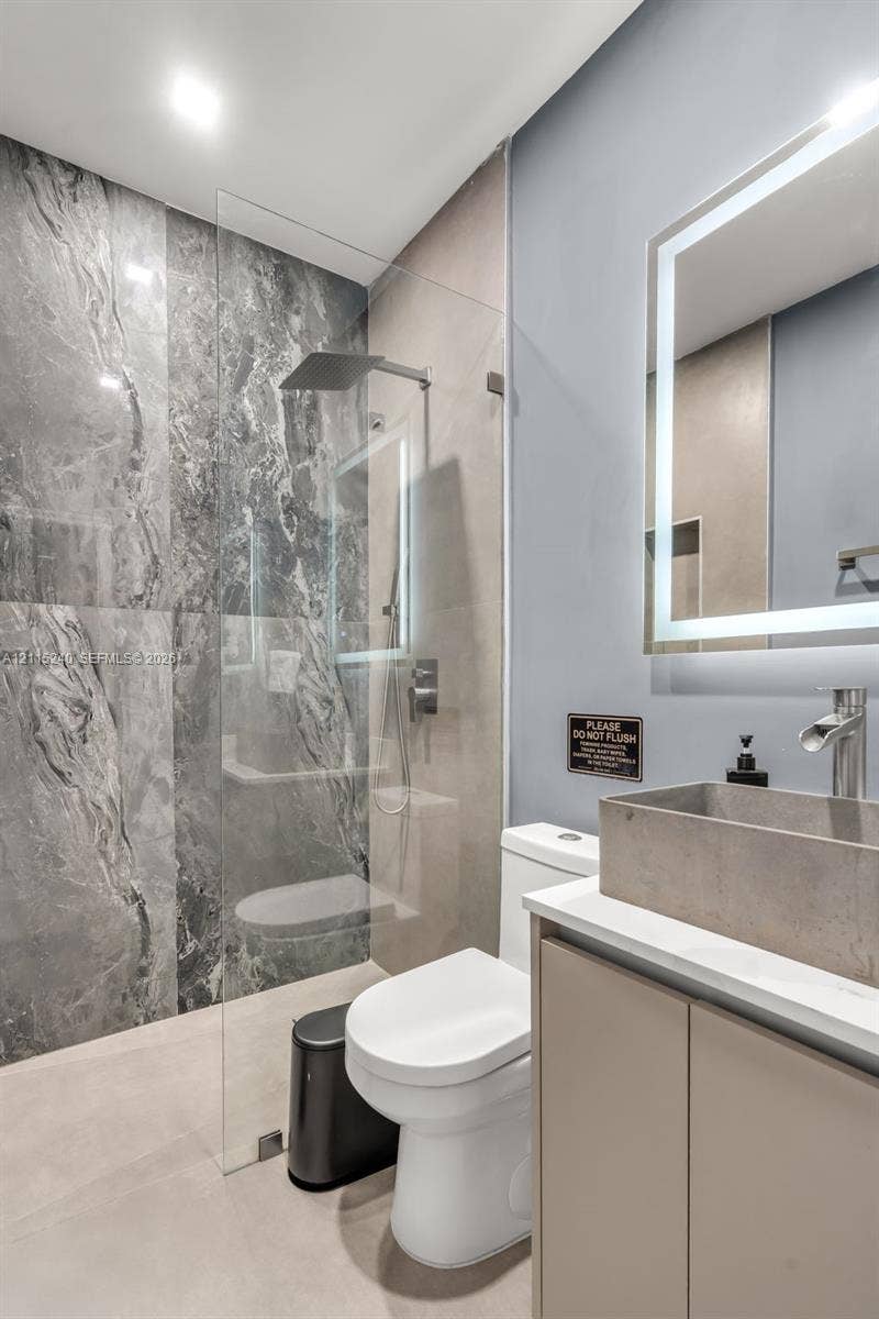 Walk-in shower with floor-to-ceiling stone-patterned tile, frameless glass panel, and rainfall showerhead