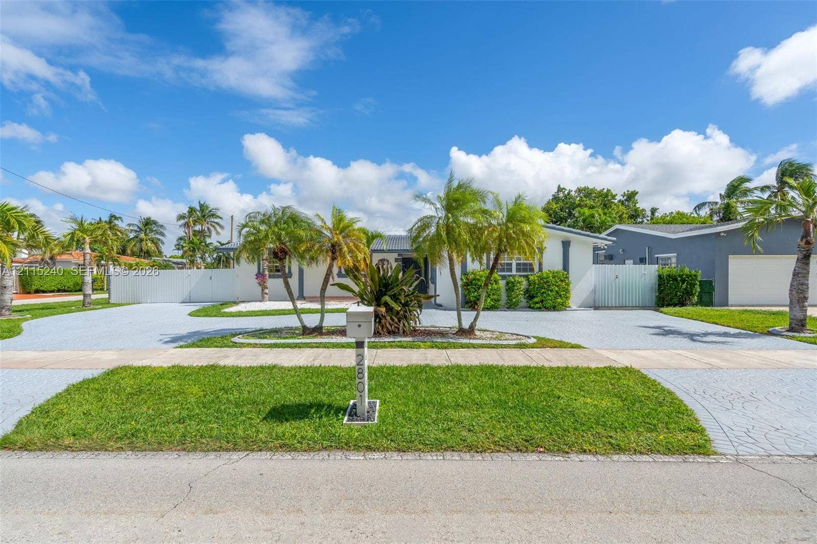 Single-story exterior featuring a stamped concrete driveway, lush palm tree landscaping, and perimeter privacy fencing