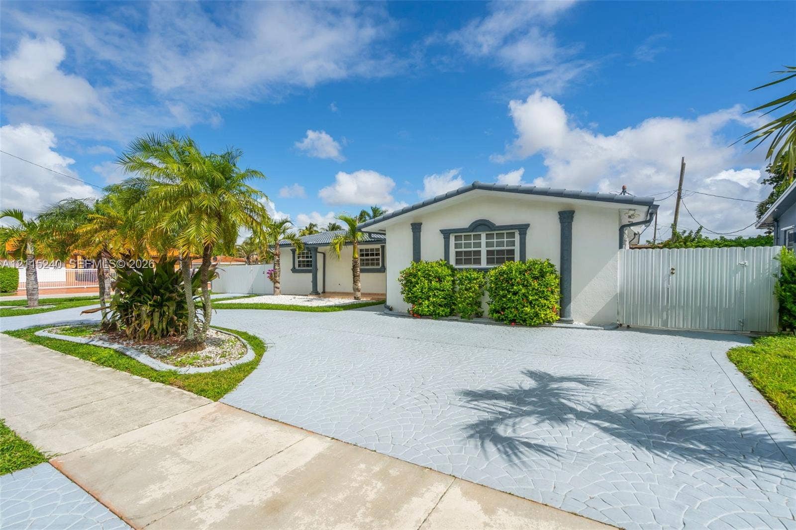Single-story exterior featuring light-toned stucco walls, contrasting window trim, decorative columns, textured concrete driveway, and white privacy fencing