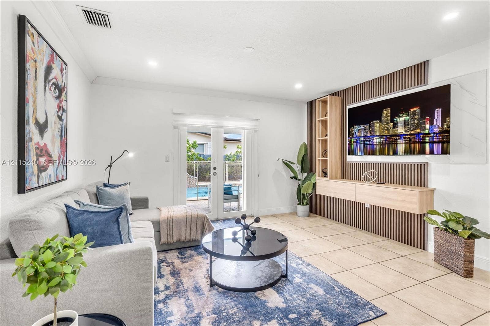 Living area featuring a custom media wall with vertical wood slats, built-in light wood cabinetry, recessed lighting, tile flooring, and glass-paned double doors