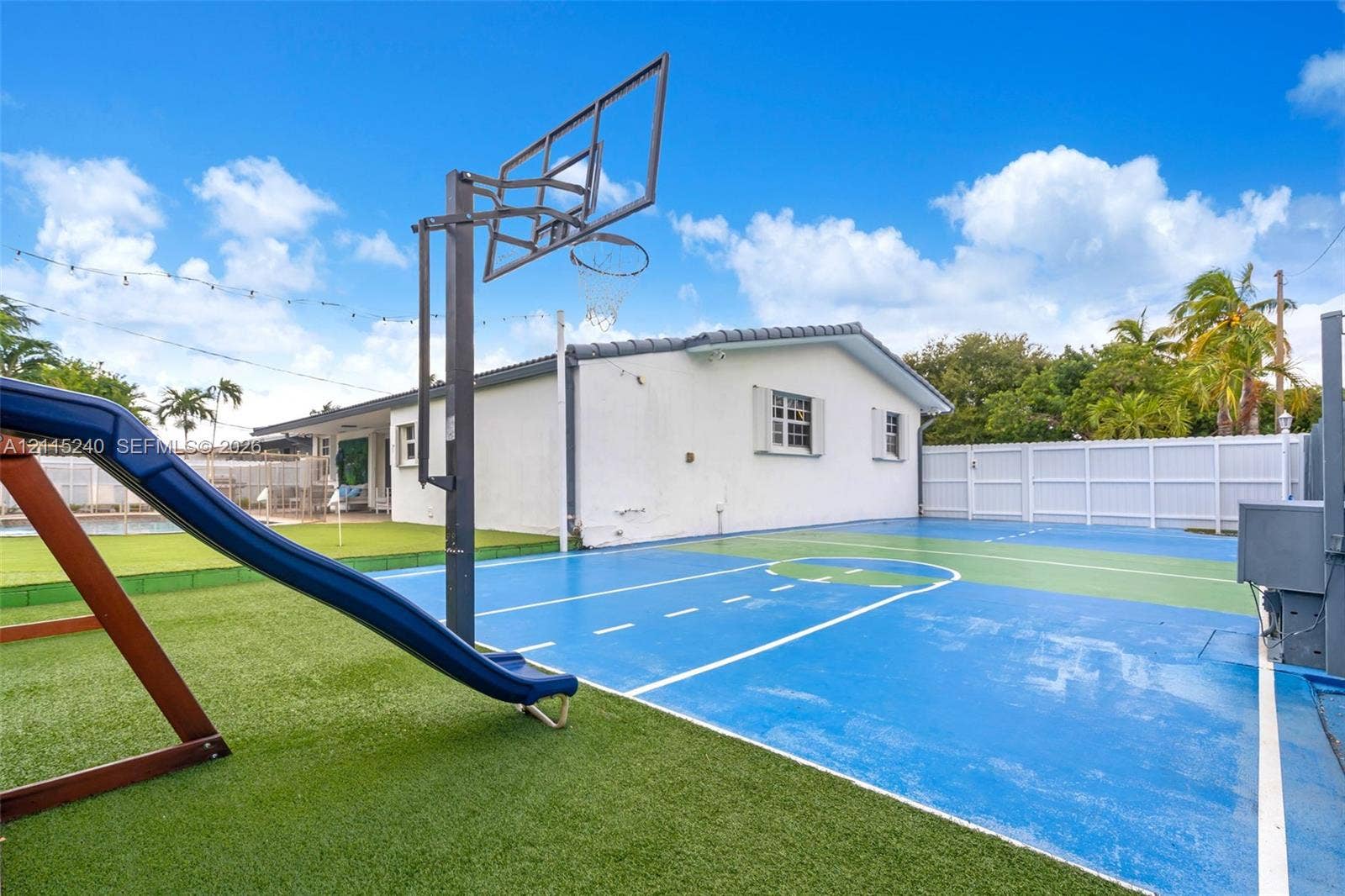 Outdoor recreation area featuring a multi-sport court with a built-in basketball hoop, synthetic turf, and perimeter fencing