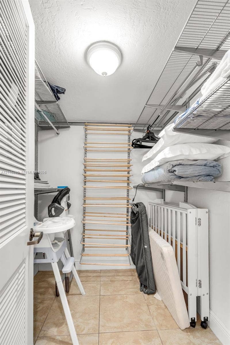 Storage area featuring tile flooring, louvered door, integrated metal shelving, and a wall-mounted wooden shoe rack