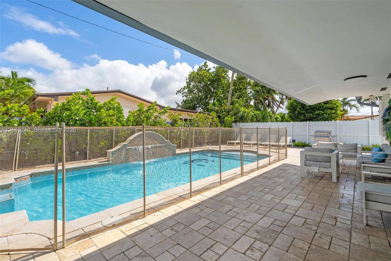 Covered patio with paver flooring, swimming pool with integrated water feature, and perimeter privacy fencing