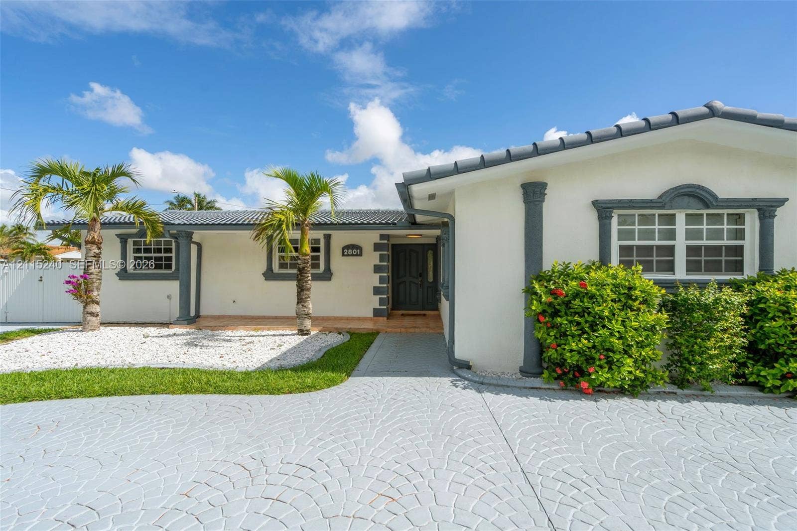 Exterior facade featuring light-colored stucco, contrasting trim, decorative columns, a tiled roof, and a patterned concrete driveway