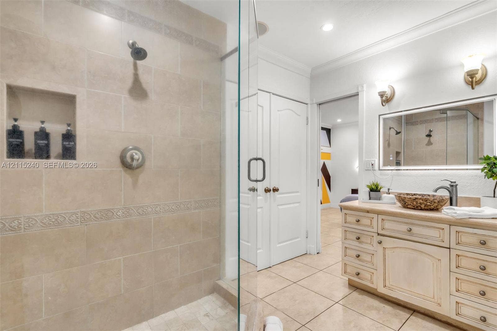 Walk-in shower featuring floor-to-ceiling tile, a built-in recessed storage niche, and a glass enclosure, paired with a custom vanity cabinet and framed vanity mirror