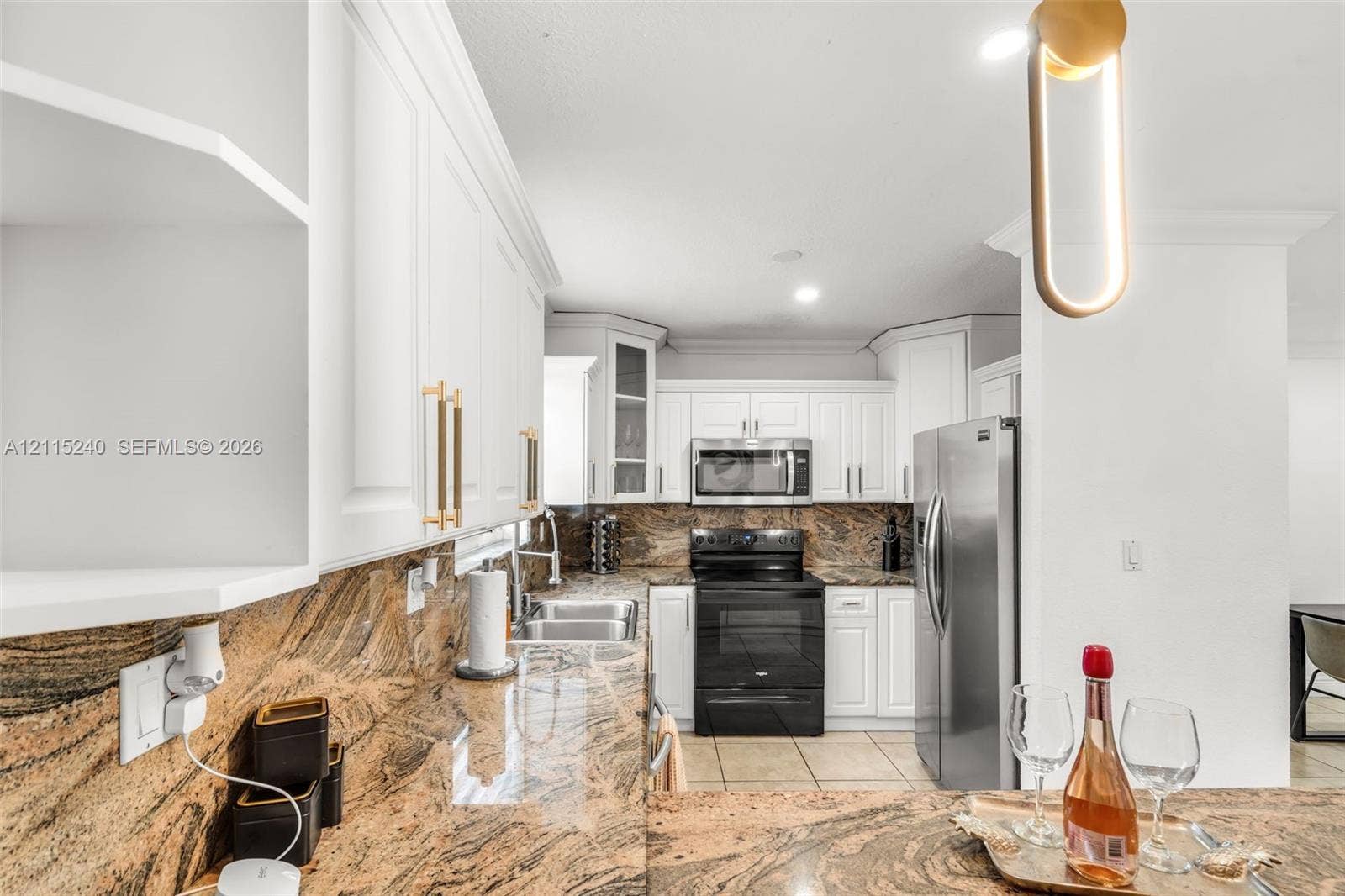 Kitchen featuring white cabinetry with gold-tone hardware, stone countertops, stainless steel appliances, and contemporary pendant lighting