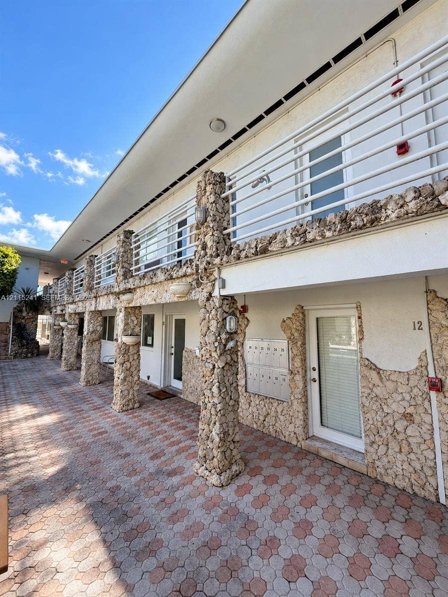 320 85th Street, #22, Miami Beach, FL 33141 Exterior facade featuring natural stone columns, multi-level walkways, stone masonry accents, a paved patio, and metal railings
